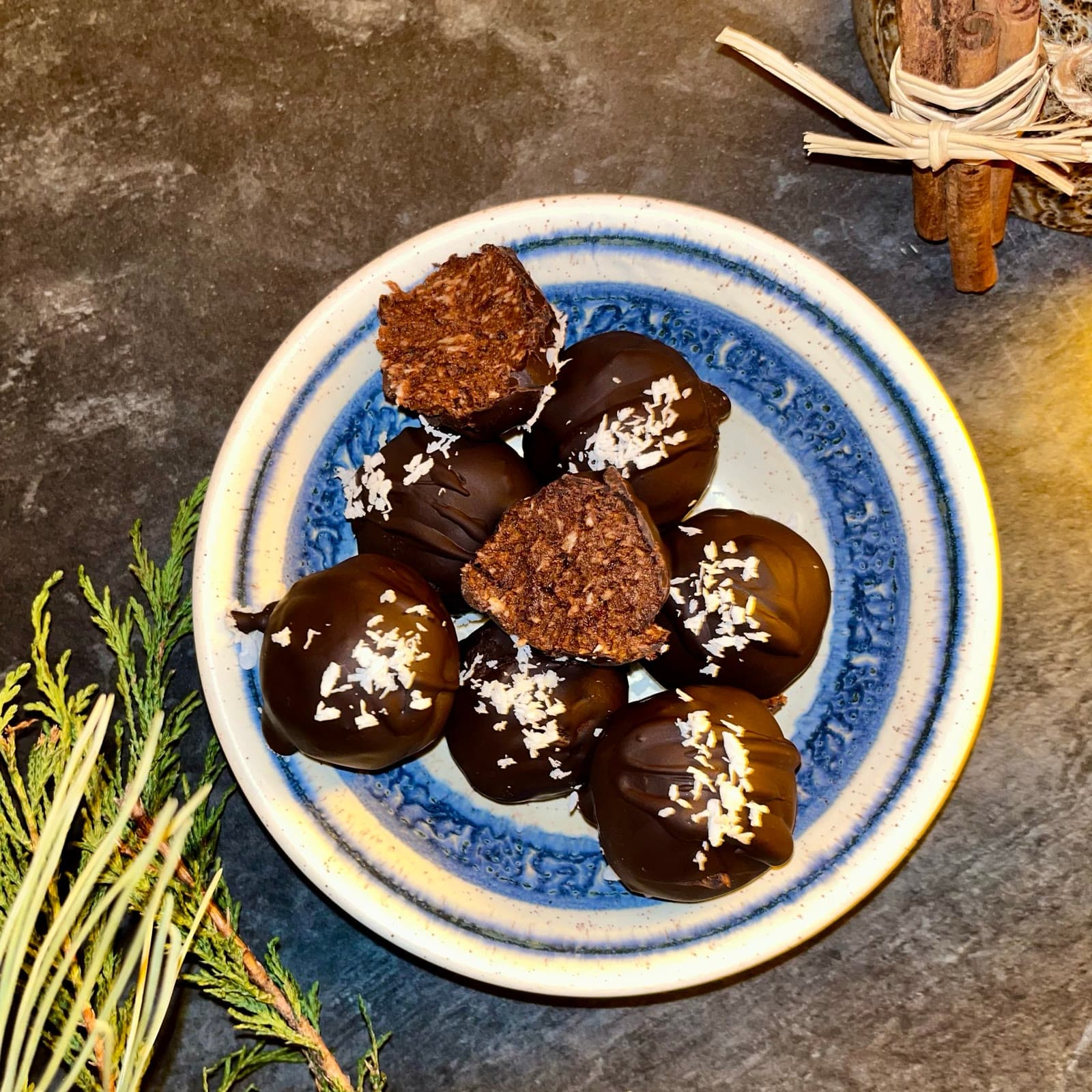 Chocolate coated truffles sprinkled with coconut on a blue rimmed plate, one broken open