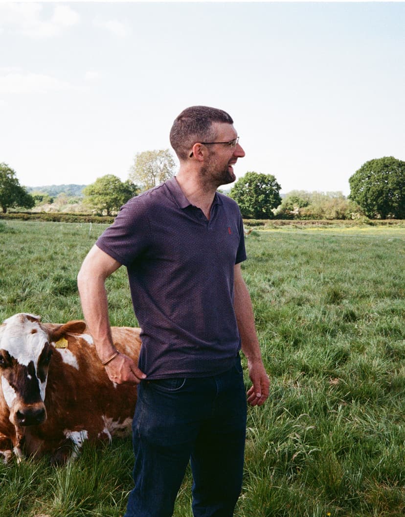 A farmer standing with his cow in the pasture