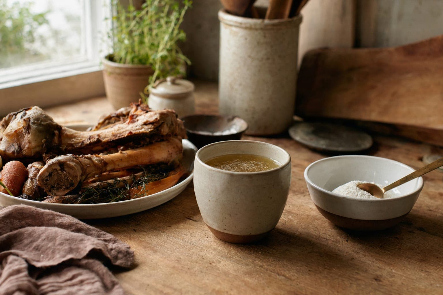 A rustic table with a bowl of broth, bread and ingredients in soft light