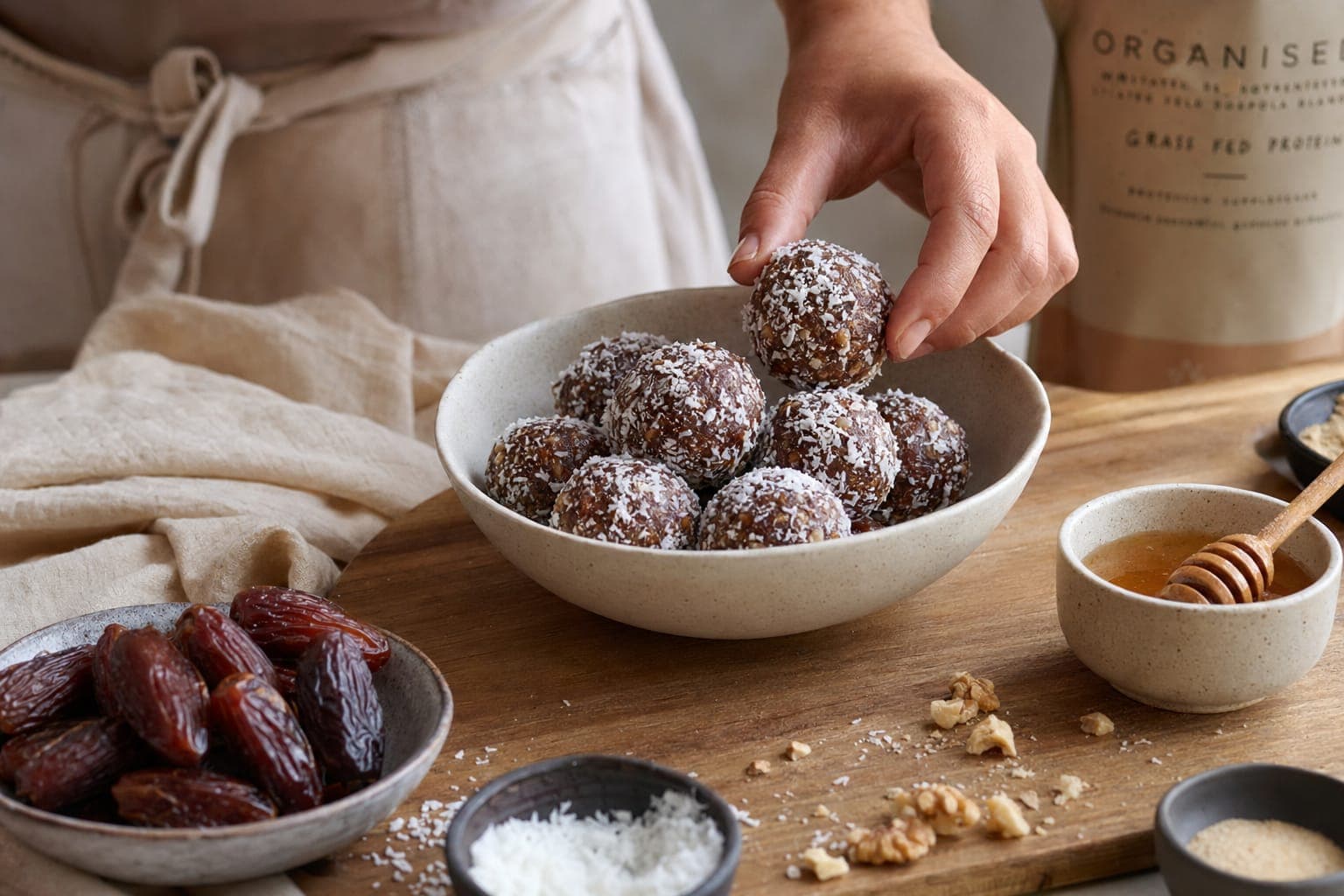Hands rolling date and honey energy balls in a bowl on a counter