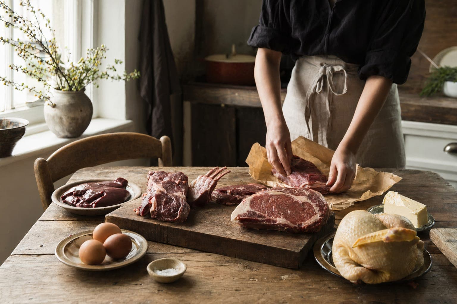 A woman preparing raw meat at a kitchen counter in soft light