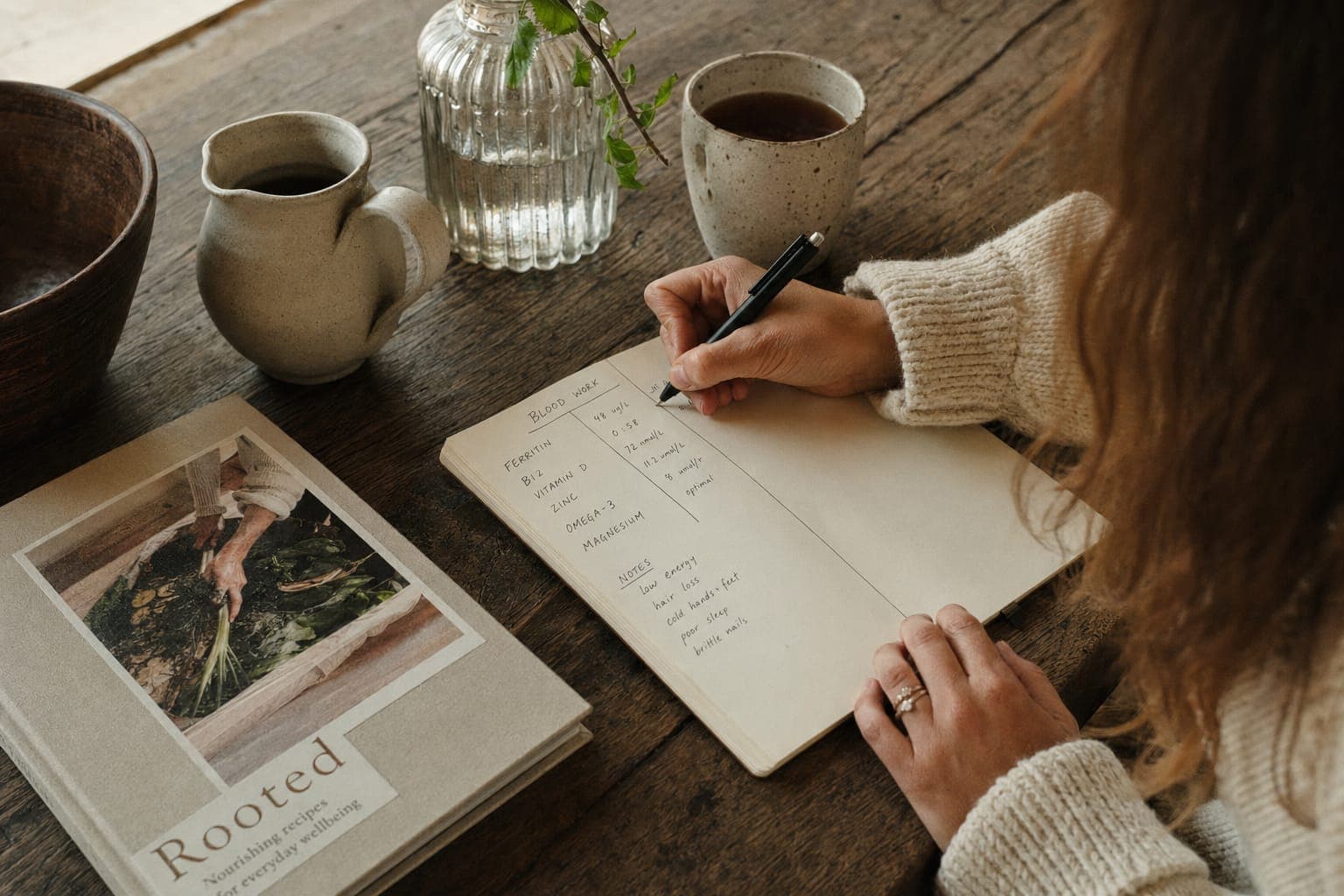 A person reading a book with a mug at a table in soft light