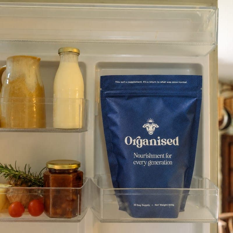 An Organised pouch standing in the fridge door, beside a bottle of milk, a jug and a jar