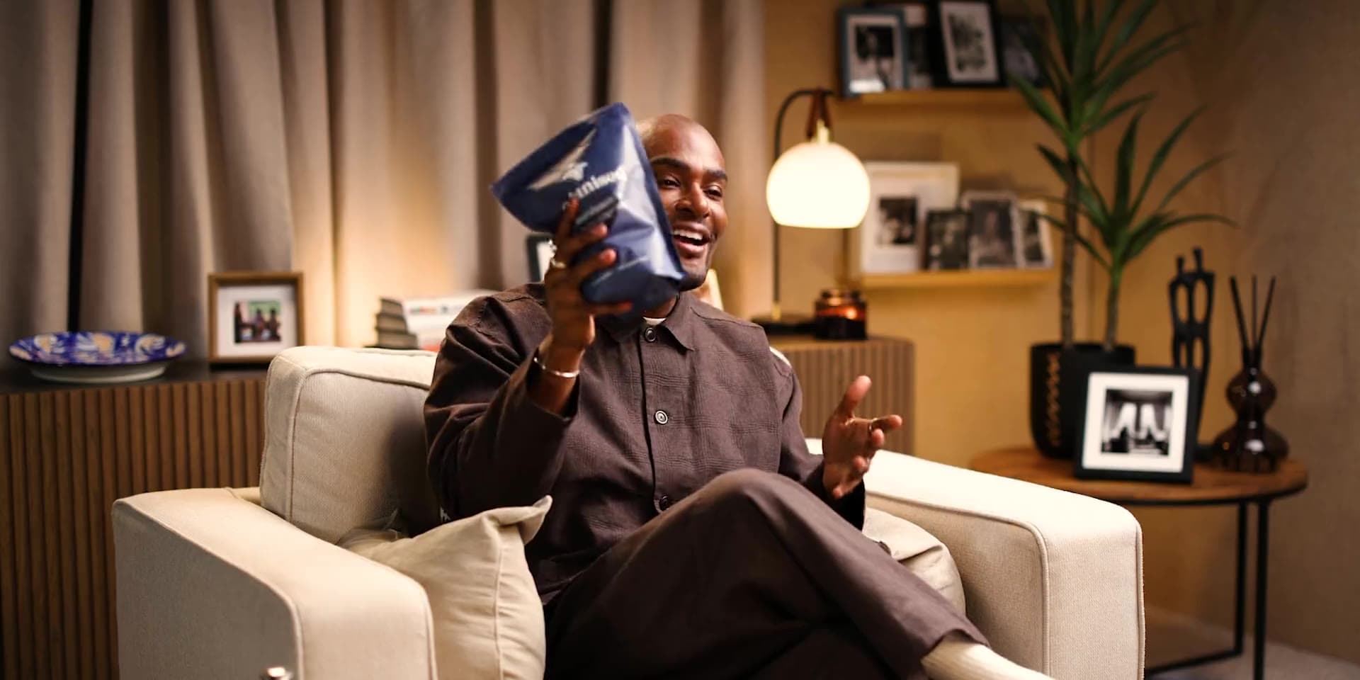 Paul Brunson in an armchair, laughing, holding an Organised pouch up beside his face