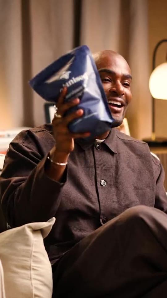 Paul Brunson in an armchair, laughing, holding an Organised pouch up beside his face