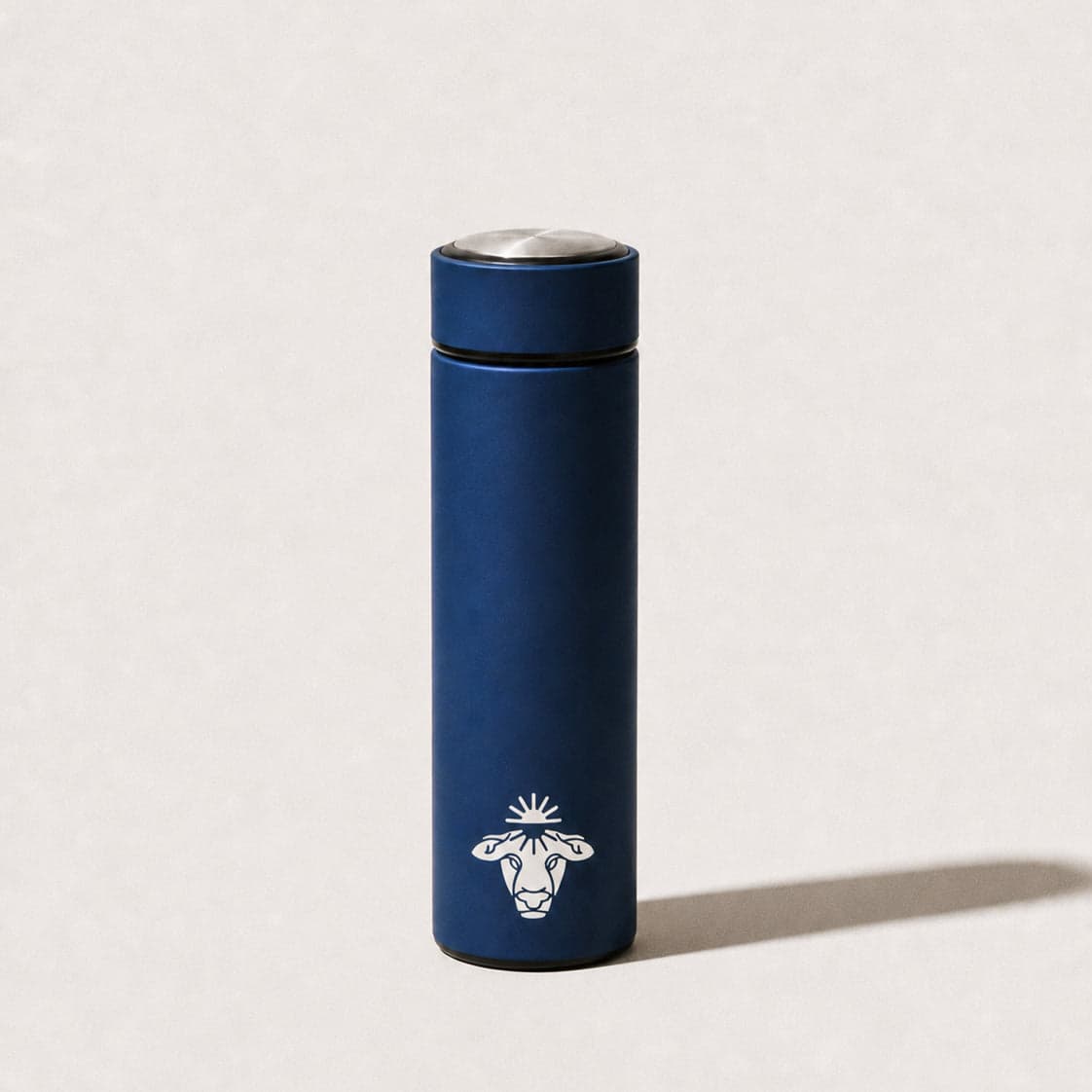 The Organised stainless steel bottle in navy, with the white cow mark, photographed on a cream background