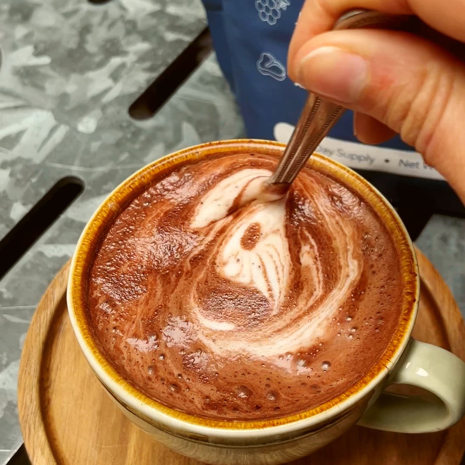A hand stirring a warm mug of Organised, the pouch behind