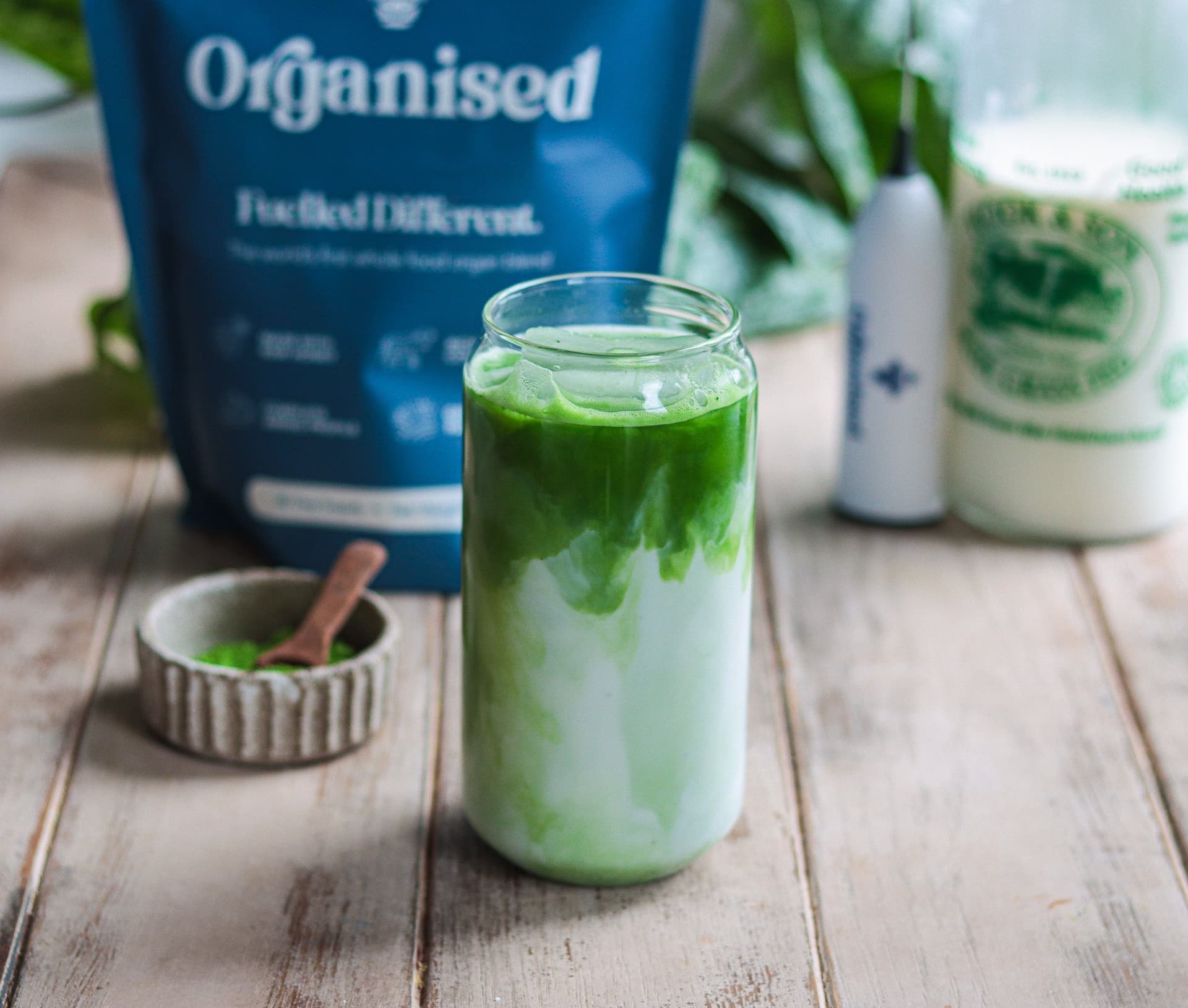 An iced matcha swirling into raw milk in a tall glass
