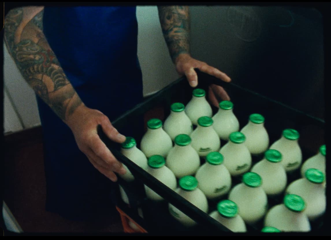 A farmer carries a crate of fresh milk bottles with green caps