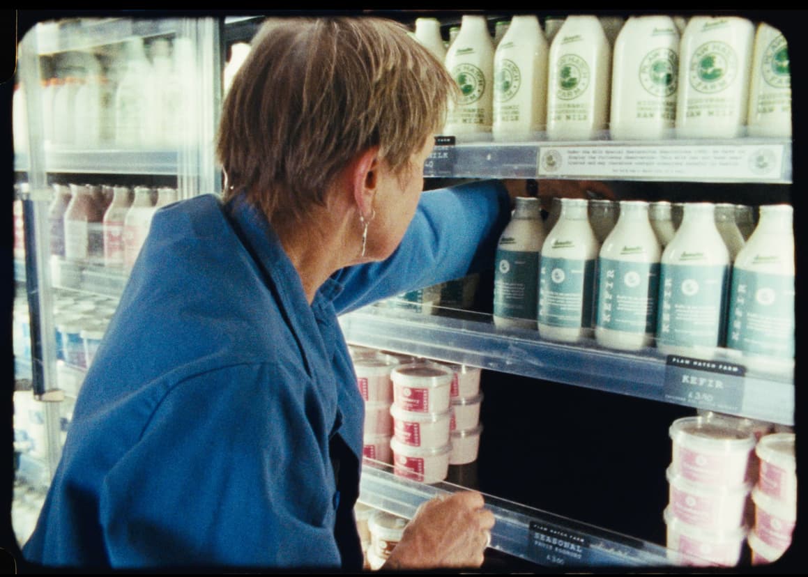 A hand reaching for a bottle of raw milk in the farm fridge