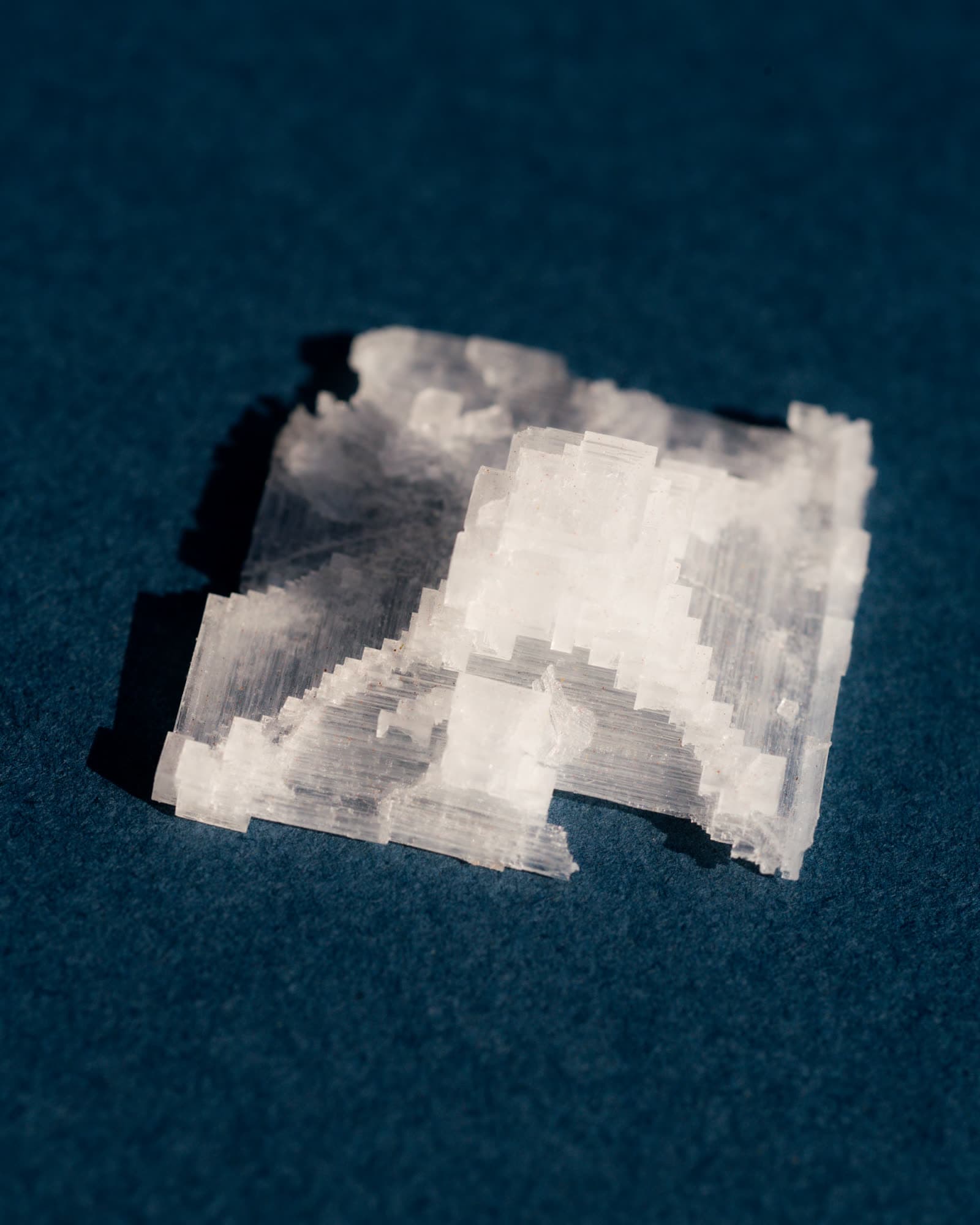 A single flake of sea salt, stepped like a ruin, lit hard on deep navy paper